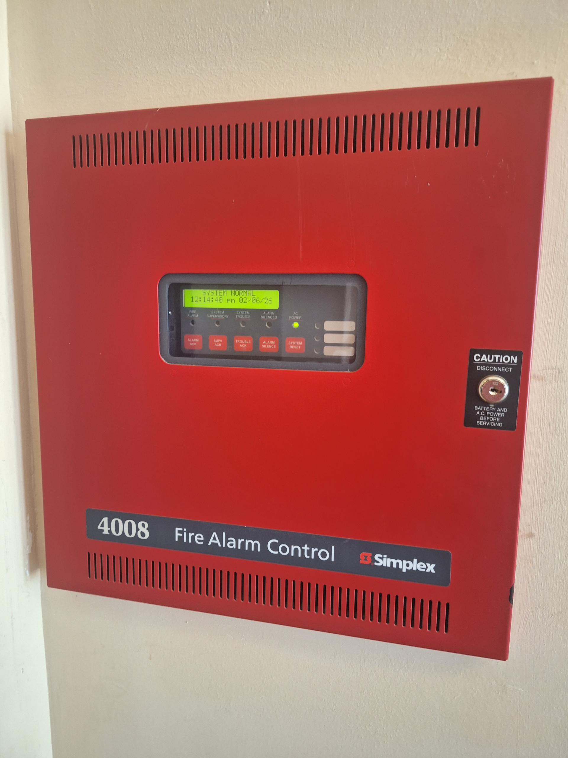A commercial fire alarm control panel displaying a yellow trouble signal LED in an Austin office building. Service tag shows Firetrol Protection Systems.