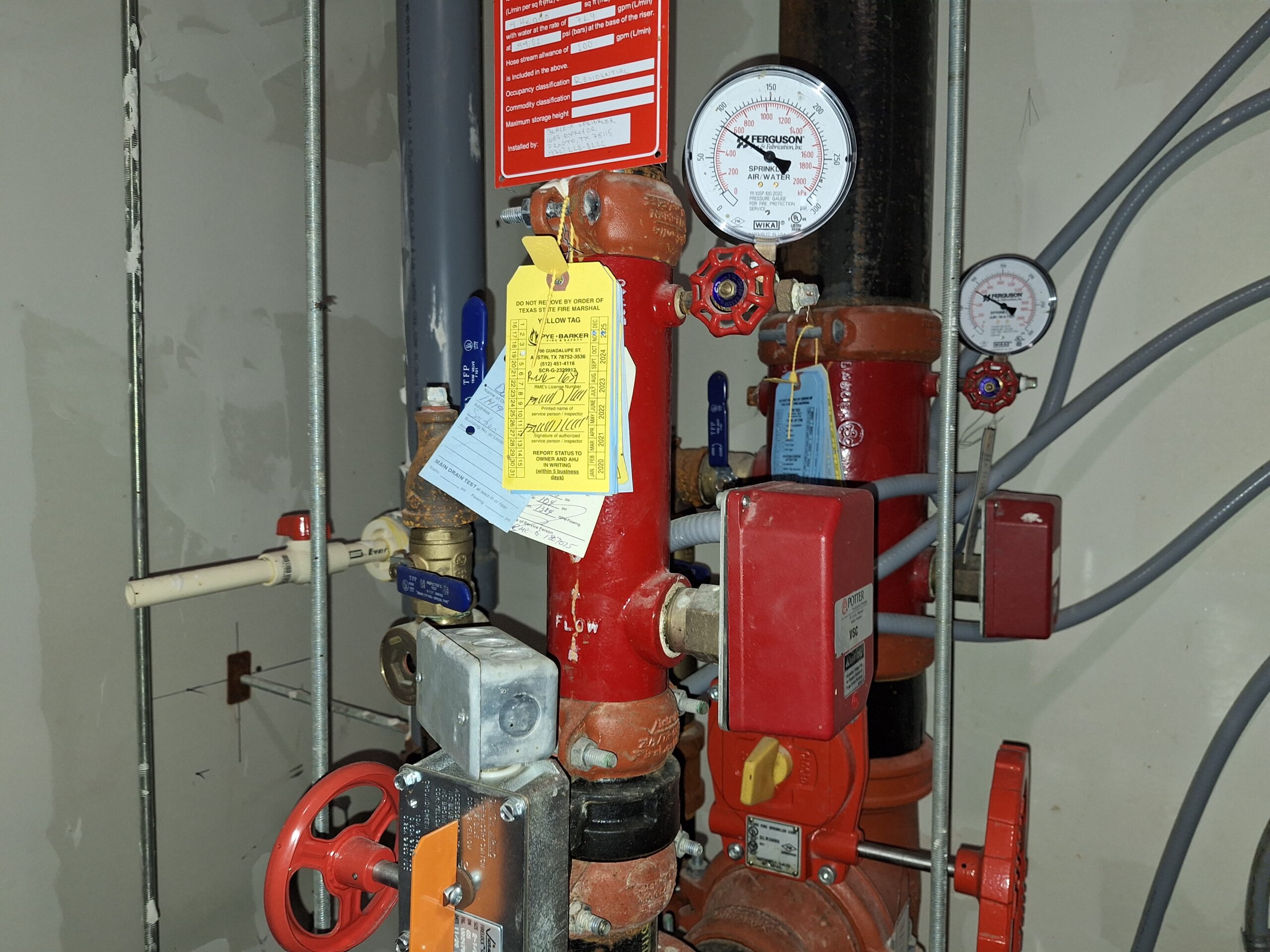 A commercial fire alarm technician inspecting a waterflow switch on a sprinkler pipe in Austin, Texas.