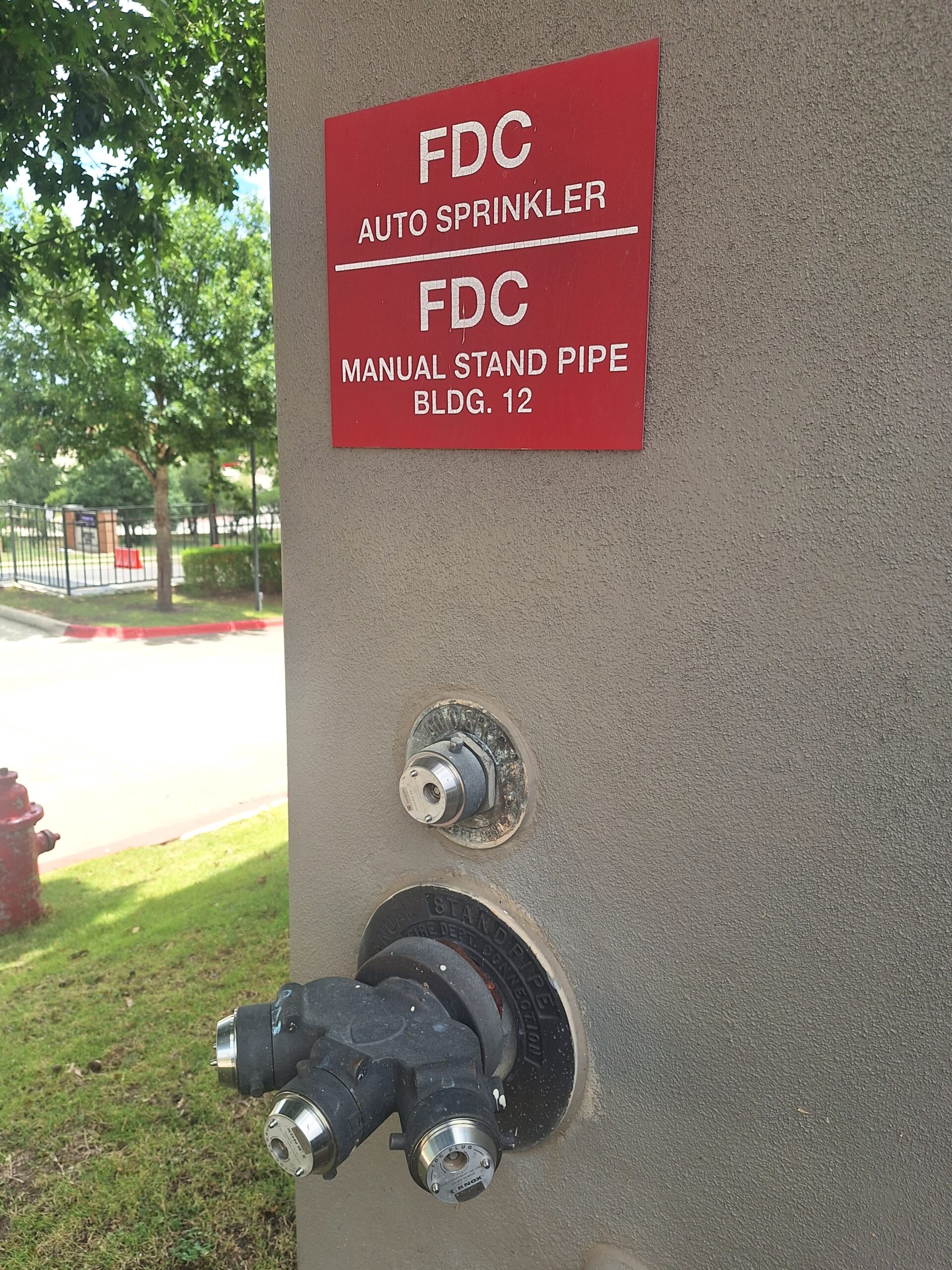 A commercial Fire Department Connection and Knox Box mounted on a stucco wall in Austin, Texas.